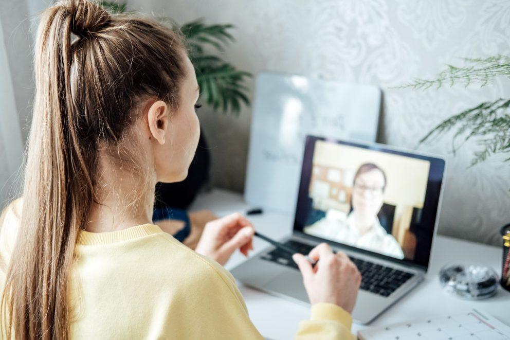 Mädchen sitzt zuhause am Schreibtisch vor ihrem Computer und führt ein Onlinebewerbungsgespräch durch