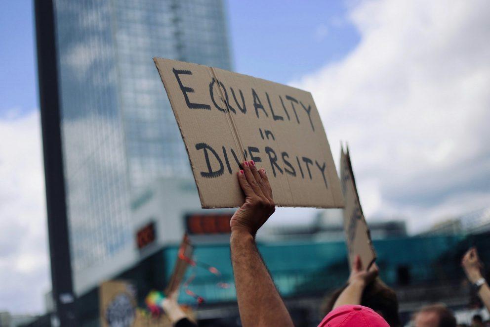 Mehr Diversität am Arbeitsplatz. Das Bild zeigt zwei Hände, die ein Plakat hoch halten wo "Equality in Diversity" drauf steht. Das bedeutet frei übersetzt soviel wie Gleichheit in Vielfalt.